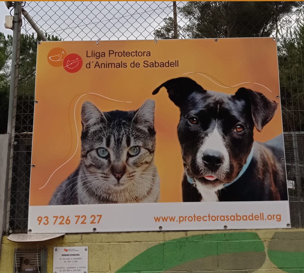 Cartel de la Lliga Protectora d'Animals de Sabadell con un gato y un perro en la entrada de su refugio